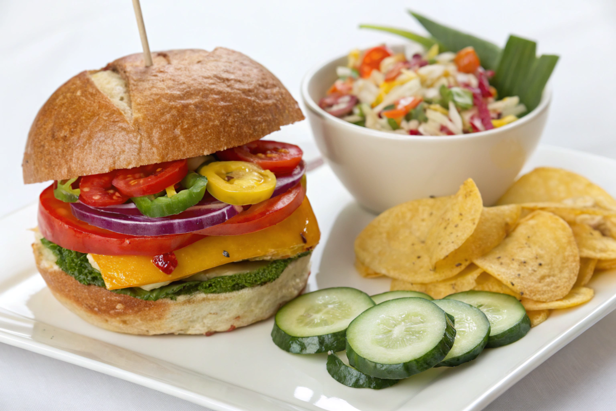 A Colorful Veggie Sandwich layered with fresh lettuce, tomatoes, cucumbers, carrots, and hummus on whole-grain bread, served with a side salad.