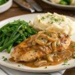 "Craig Claiborne’s Smothered Chicken served with rich onion gravy, garnished with parsley, alongside mashed potatoes and green beans."